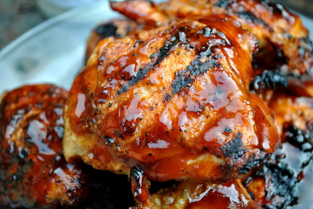 Barbecue chicken thighs slathered with barbecue sauce on a plate on a picnic table