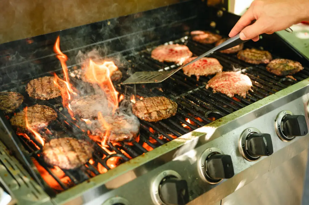 Man using a stainless steel spatula to flip hamburgers cooking on a gas barbecue grill