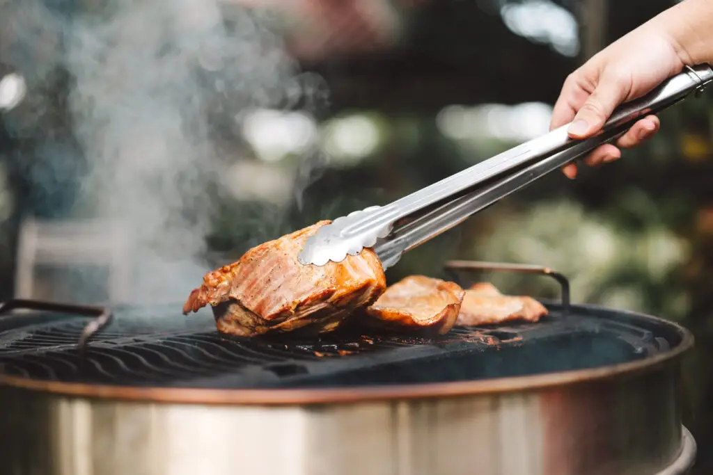 Woman flipping barbecue chicken breasts on a charcoal grill with stainless steel tongs