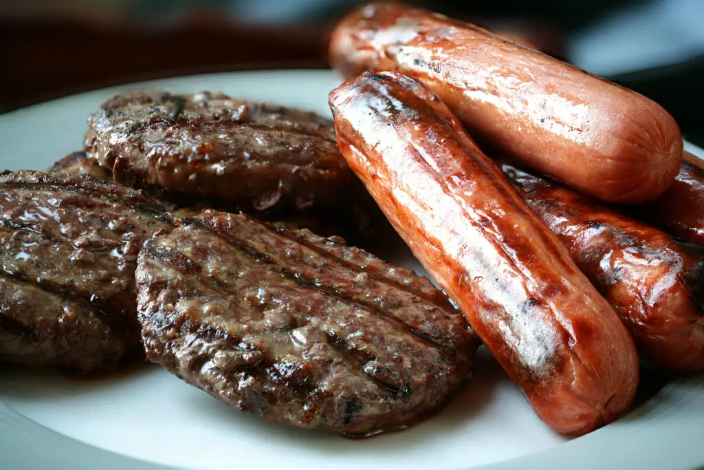 A close-up of grilled hamburgers and hot dogs resting on a white serving plate