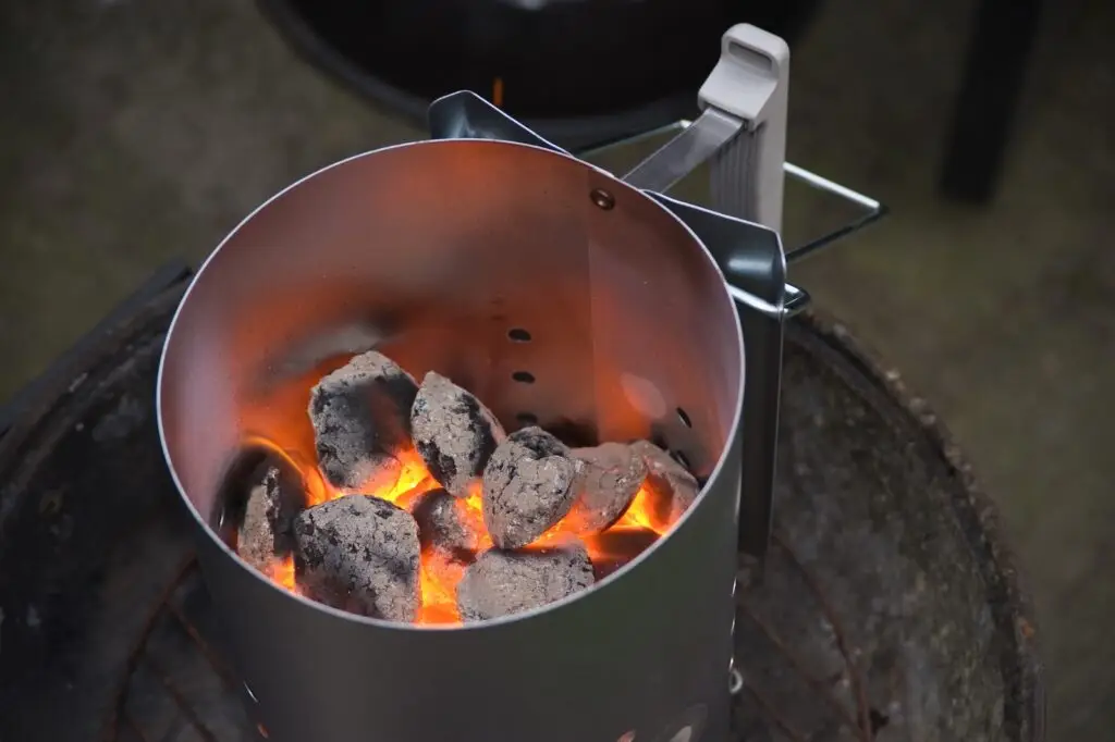 Charcoal chimney starter half filled with hot charcoal briquettes