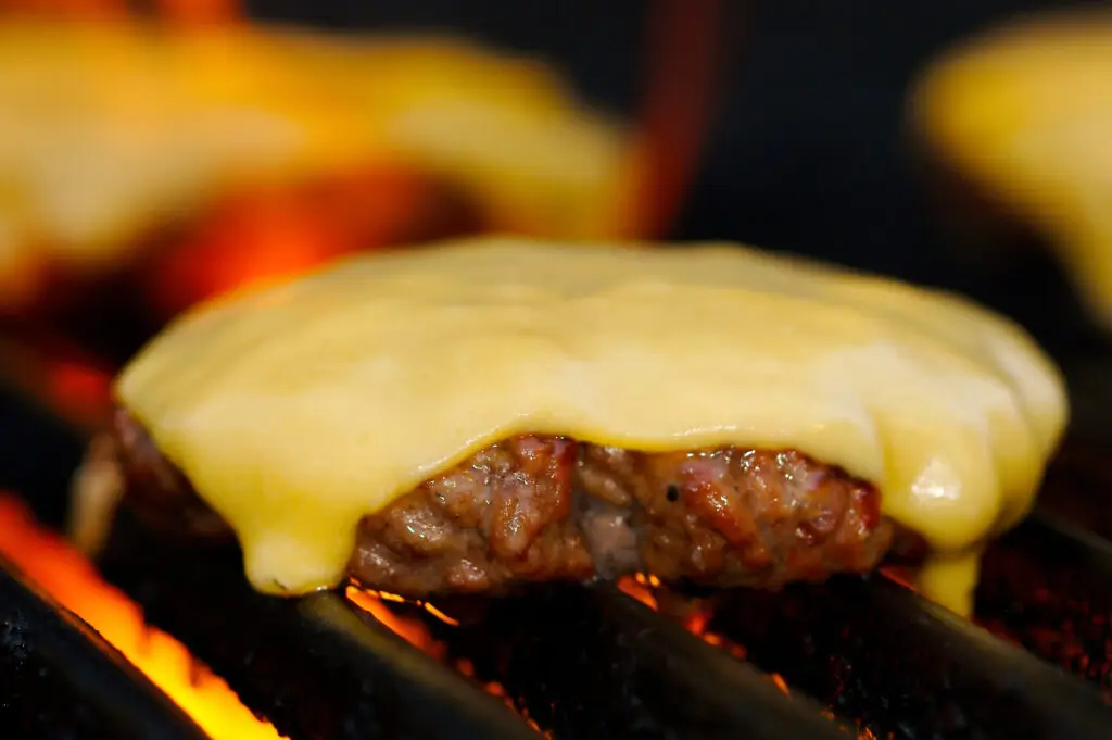 A close-up of a cheeseburger cooking on a gas grill