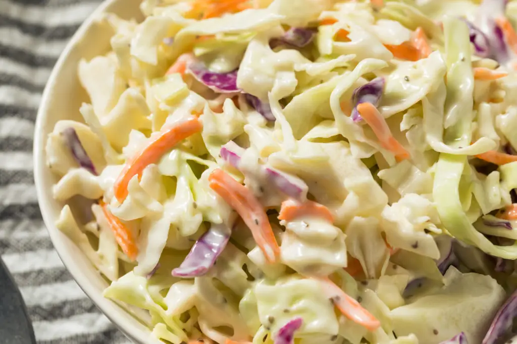 Homemade creamy coleslaw in a white serving bowl on a picnic table