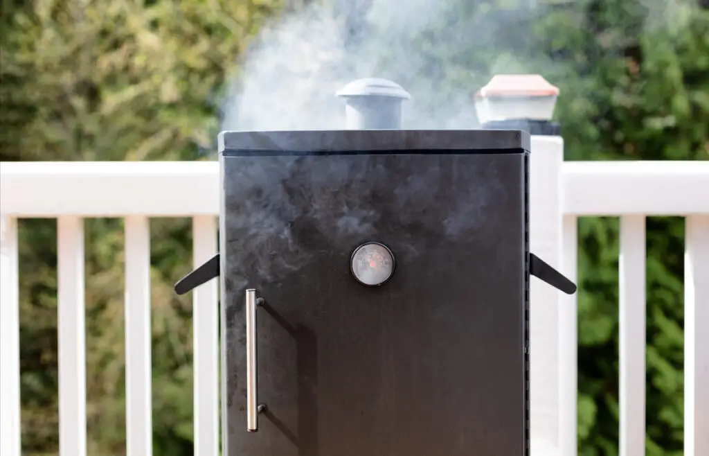 An electric smoker, smoking on a deck in a backyard
