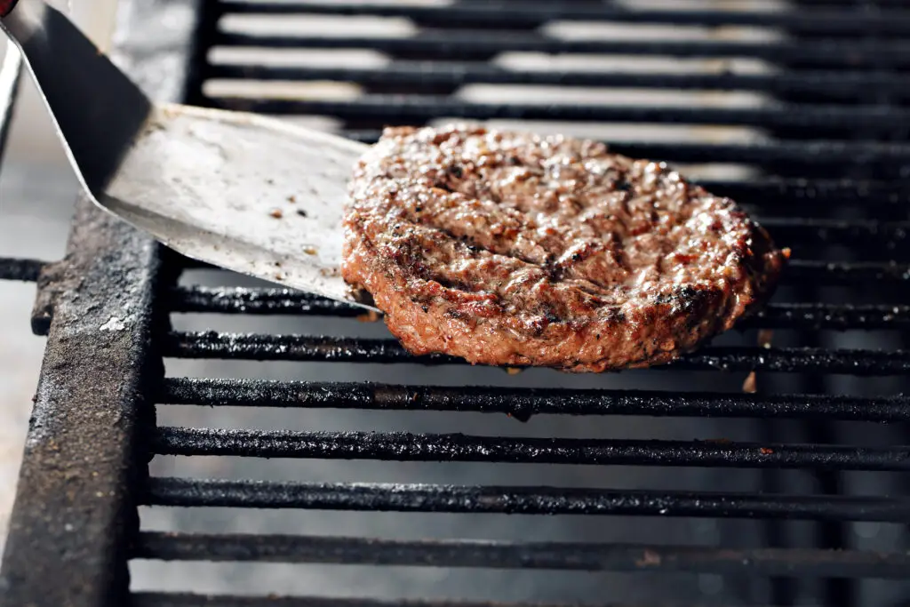 A hamburger being flipped on a grill with a spatula