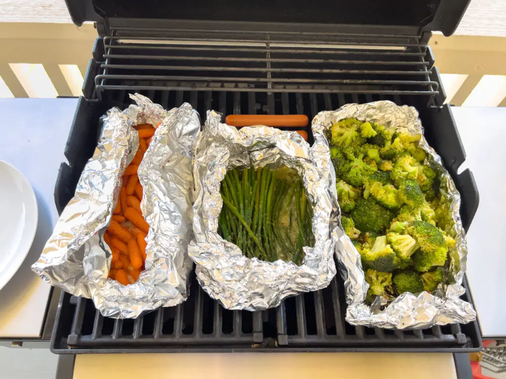 Grilled carrots, asparagus, and broccoli in foil packages on a gas grill in the backyard