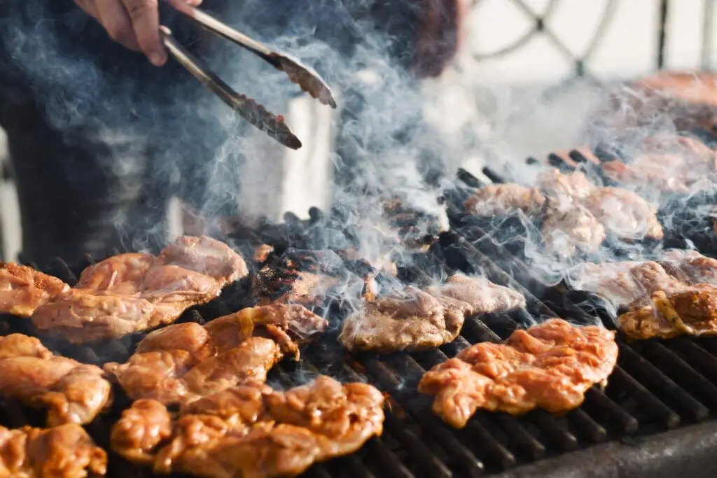 A man grilling chicken on a charcoal grill with tongs