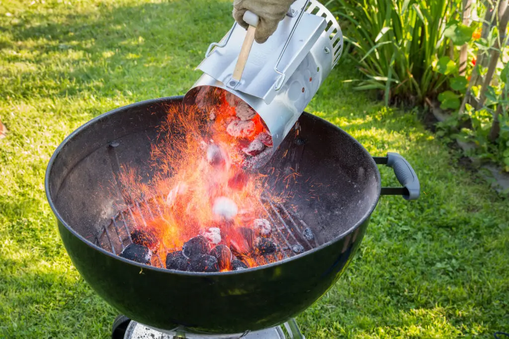 Emptying hot charcoal from a starter chimney into a kettle grill in the backyard
