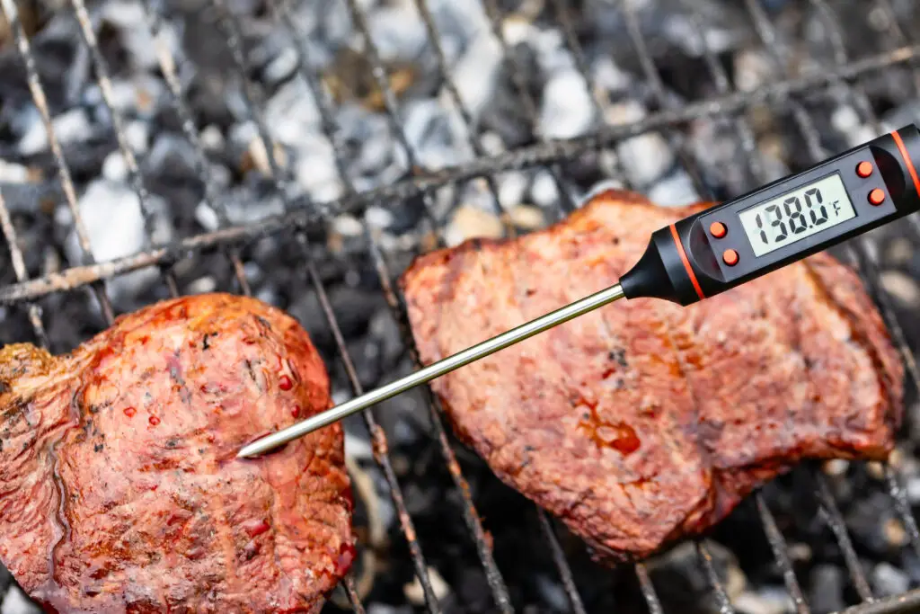 Using a digital meat thermometer to check the temperature of grilled steaks on a charcoal grill
