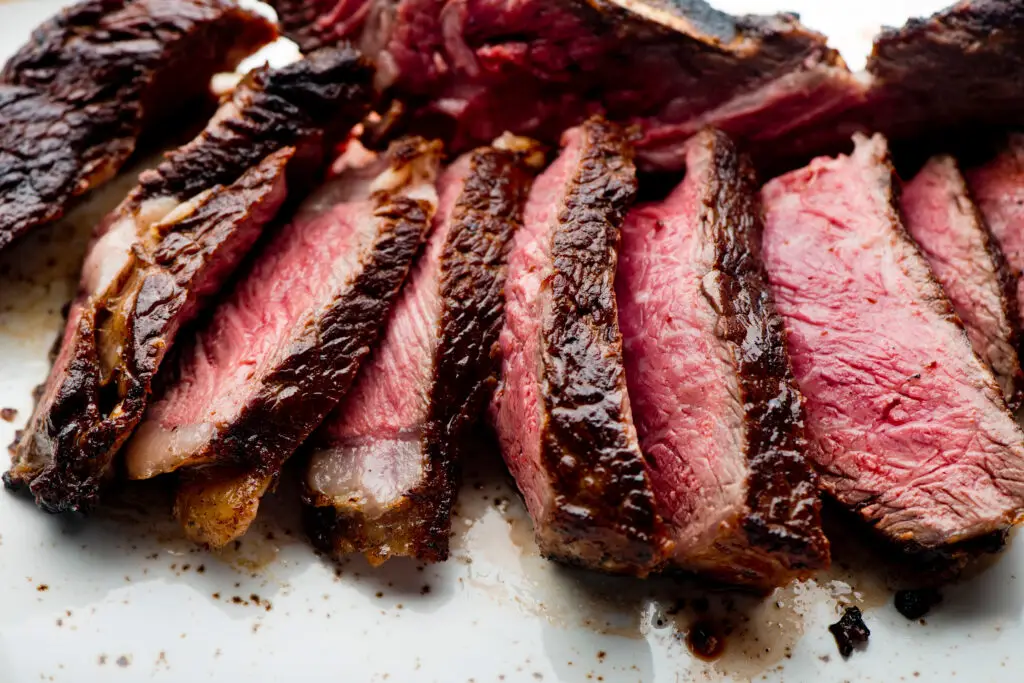 Medium rare, juicy grilled steak sliced and resting on a white serving tray