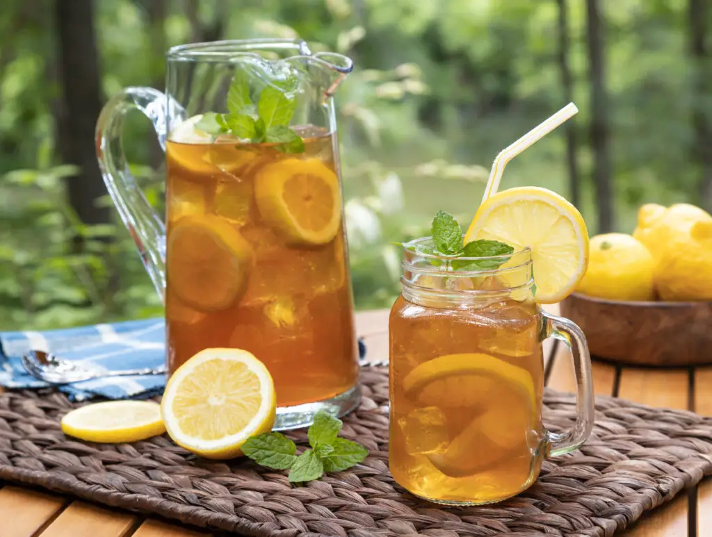 A pitcher and a glass of iced tea on a table in a backyard