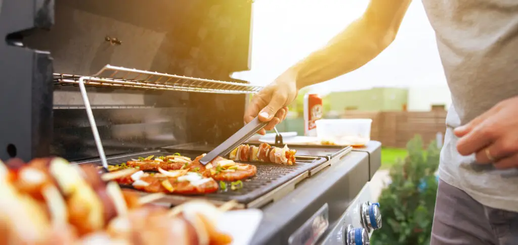 A young man grilling marinated chicken breasts and shish kebabs on a gas grill in the backyard