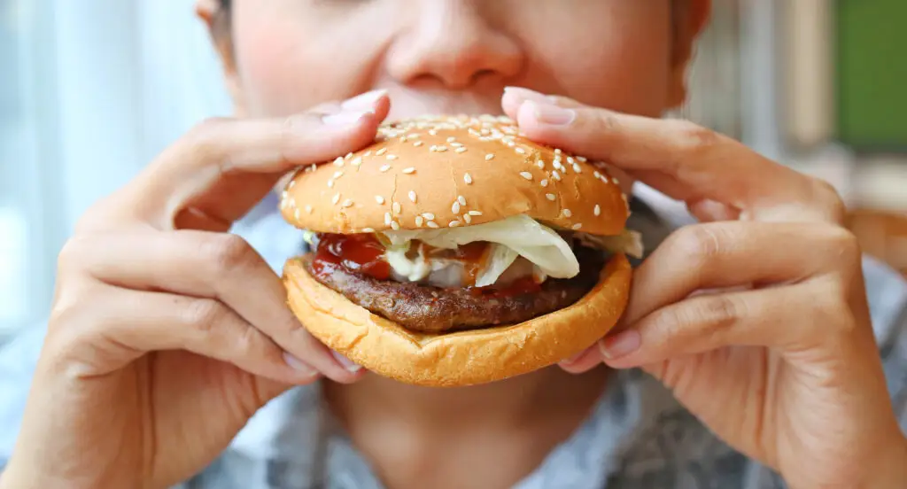 A woman eating a hamburger on a sesame seed bun