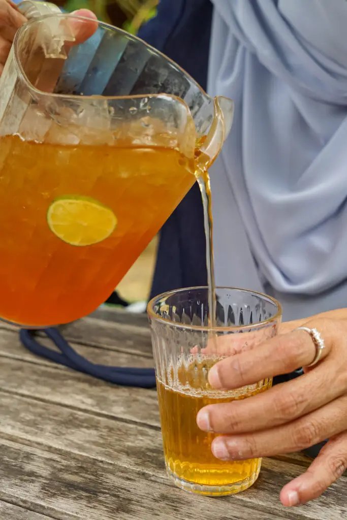 A woman pouring iced tea from a pitcher into a glass at a picnic table